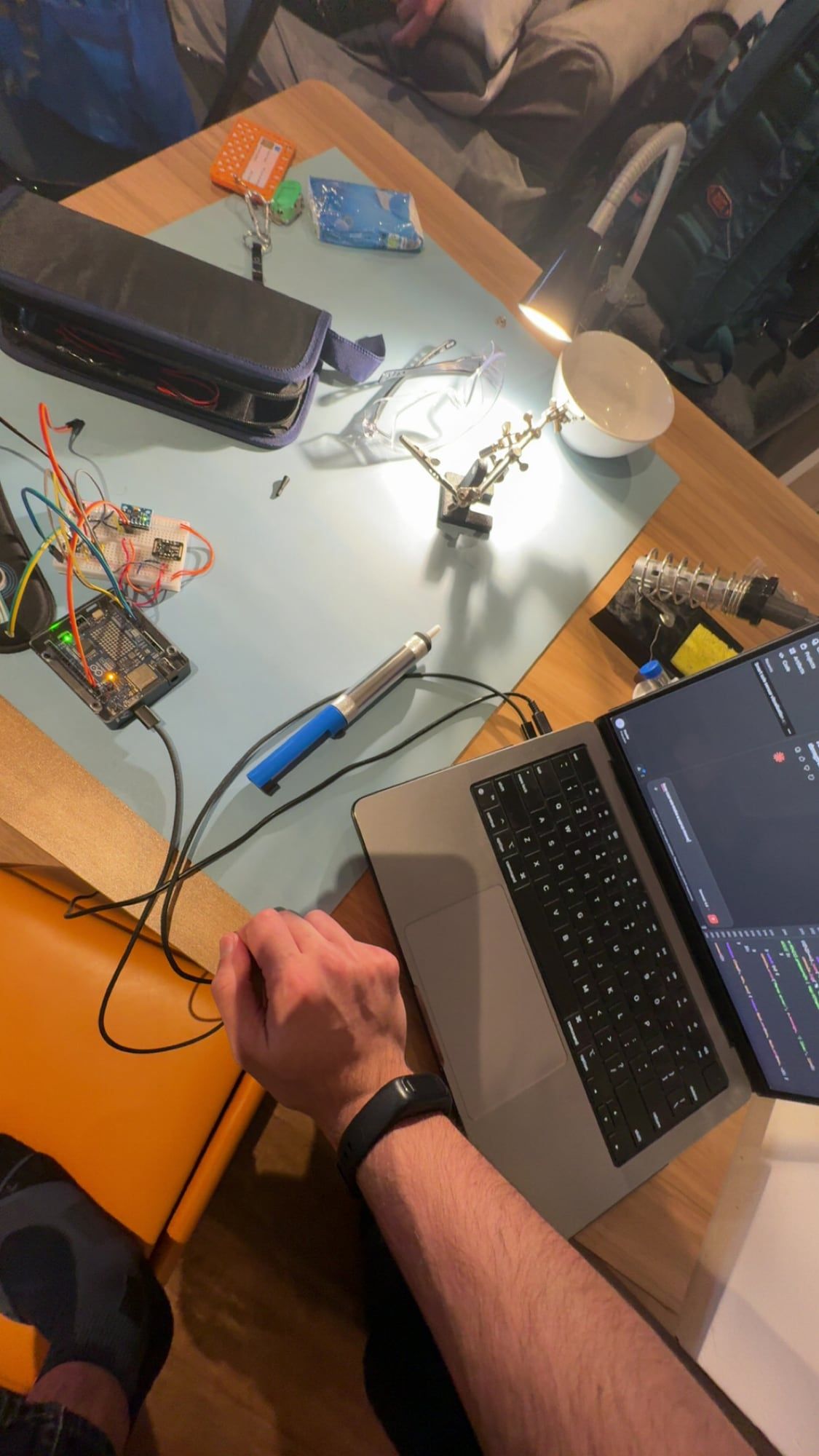 Soldering at the bench, with the Arduino and breadboard on the mat and serial output on a laptop.